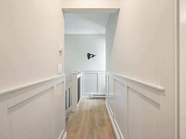 Hall with an upstairs landing, a decorative wall, light wood-style floors, a wainscoted wall, and a baseboard radiator