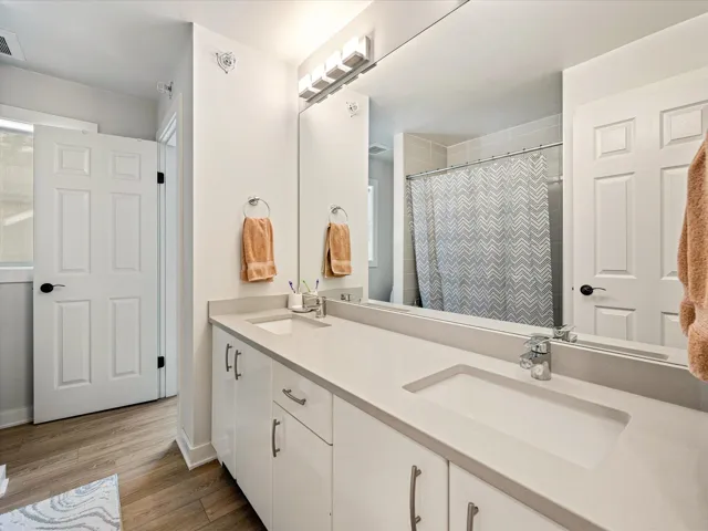Full bath with double vanity, light wood finished floors, and a shower with curtain
