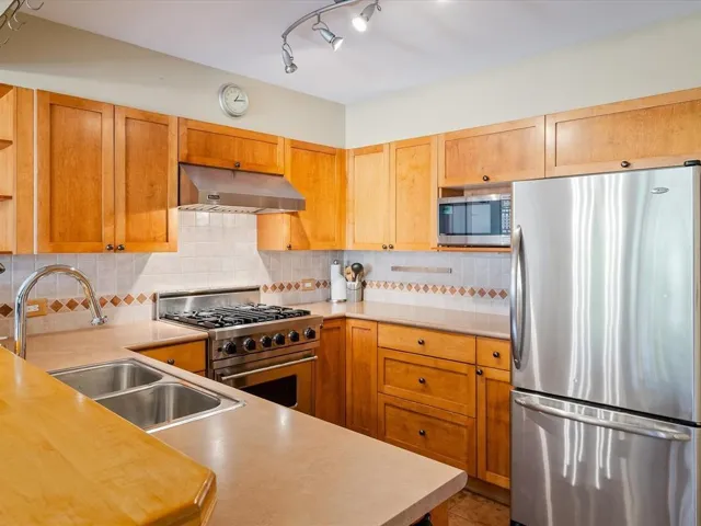 Well-appointed kitchen featuring wood cabinetry, stainless steel appliances, a gas range with an overhead exhaust hood, a double basin sink, and ample countertop space