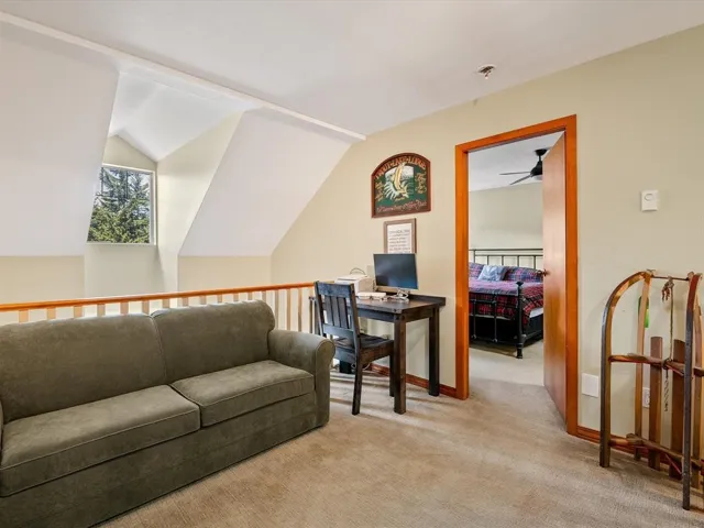 Carpeted loft area featuring a natural wood railing, sloped ceiling, and an architectural window