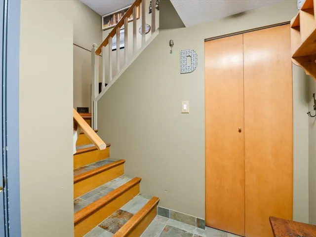Entryway featuring a staircase with wood-finish treads and tile risers, a wood handrail, white balusters, and a bi-fold closet with wood-finish doors