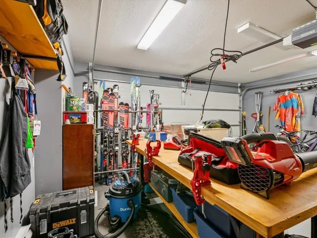 Garage interior featuring a light wood-finish workbench, overhead lighting, an exposed garage door track system, and built-in wall shelving