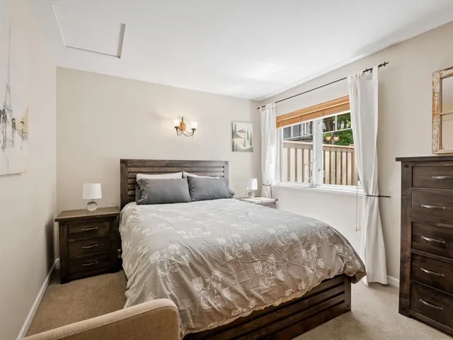 Bedroom featuring neutral wall color, carpet flooring, a multi-pane window with a light-filtering shade, and a two-light wall sconce