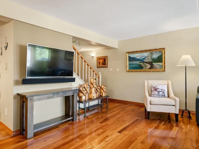 Hardwood flooring throughout a living space featuring a wall-mounted television, a soundbar, and a console table