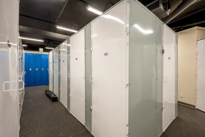 Storage facility featuring individual white and grey units, a dark ceiling with exposed ductwork, and recessed lighting
