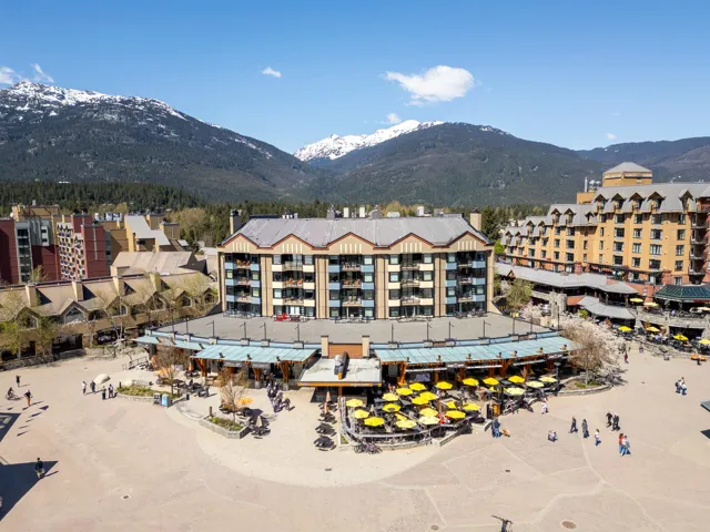 Expansive town square featuring extensive outdoor patio dining with yellow umbrellas, surrounded by multi-story buildings with balconies and traditional sloped roofs