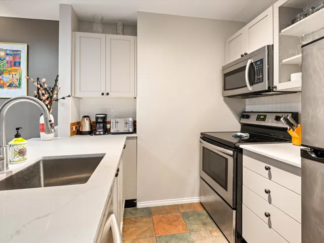 Kitchen featuring stainless steel appliances, white cabinetry, tasteful backsplash, light stone counters, and glass insert cabinets