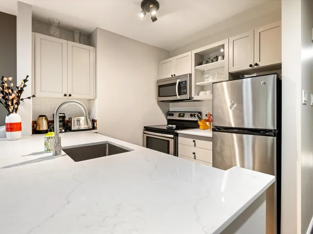 Kitchen with appliances with stainless steel finishes, light stone countertops, glass insert cabinets, white cabinetry, and backsplash