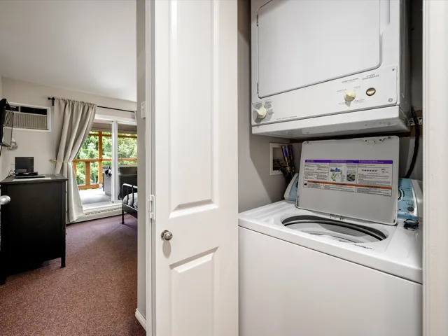 Washroom featuring dark colored carpet, a wall unit AC, stacked washer / drying machine, and a baseboard heating unit