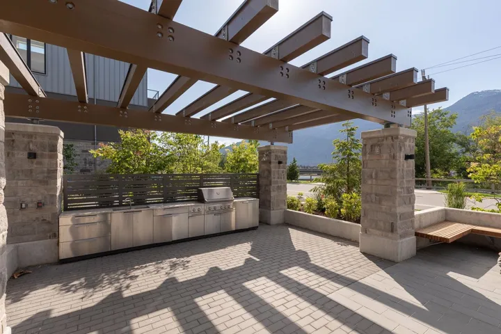 Outdoor living space featuring a substantial pergola structure with exposed beams, an integrated stainless steel outdoor kitchen with a grill and sink, and a paver patio