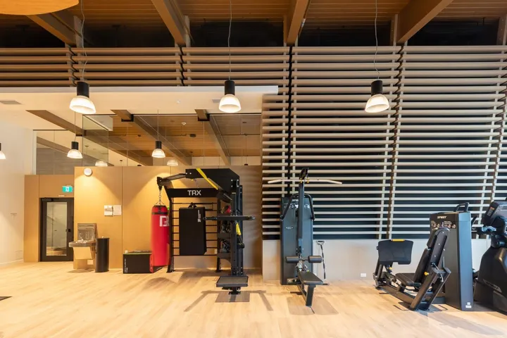 Fitness center featuring wood-finish flooring, exposed beam ceiling accents, louvered wall paneling, and mirrored wall sections