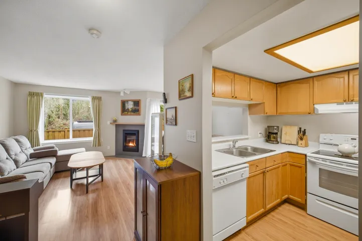 Kitchen with white appliances, light wood finished floors, open floor plan, light countertops, and a glass covered fireplace