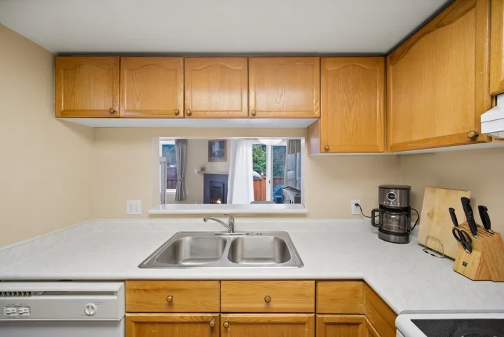 Kitchen with light countertops, white dishwasher, wood finish cabinets, and a lit fireplace
