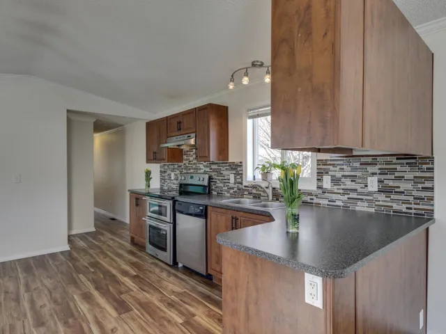 Kitchen with a textured ceiling, dark countertops, crown molding, stainless steel appliances, and wood finish cabinetry