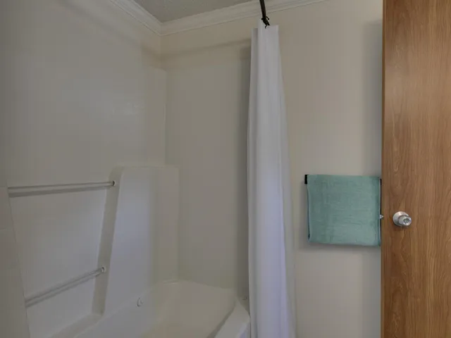 Bathroom featuring crown molding, shower / tub combo with curtain, and a textured ceiling