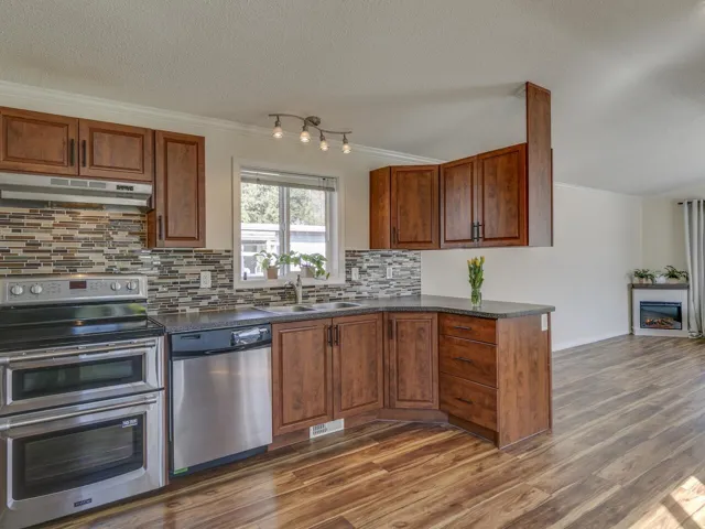 Kitchen featuring stainless steel appliances, ornamental molding, wood finish cabinetry, decorative backsplash, and dark wood finished floors