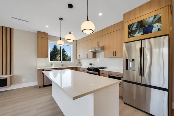 Kitchen with stainless steel appliances, a center island, hanging light fixtures, and light wood finish cabinetry