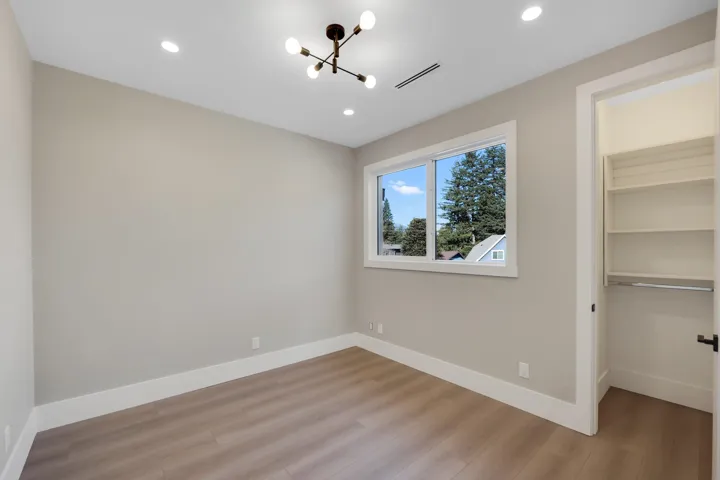 Unfurnished bedroom with a walk in closet, light wood finished floors, and suspended lighting