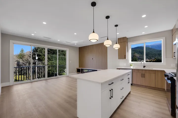 Kitchen featuring two tone cabinetry, gas stove, hanging light fixtures, light wood-style flooring, and a center island