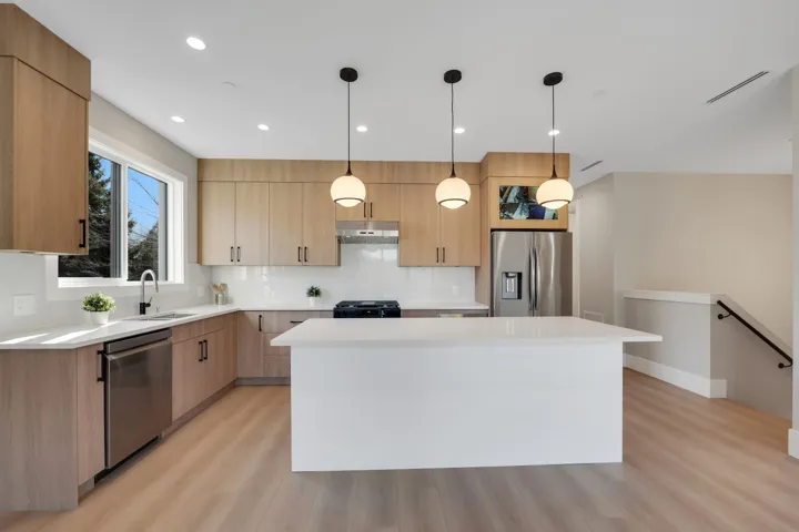 Kitchen featuring stainless steel appliances, light wood finish cabinets, a center island, decorative light fixtures, and modern cabinets