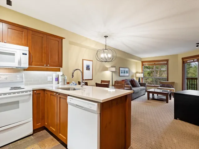 Kitchen with white appliances, brown cabinetry, tasteful backsplash, and hanging light fixtures