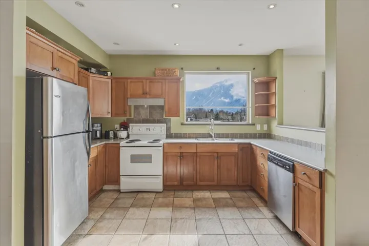 Kitchen featuring stainless steel appliances, wood finish cabinetry, light countertops, recessed lighting, and open shelves