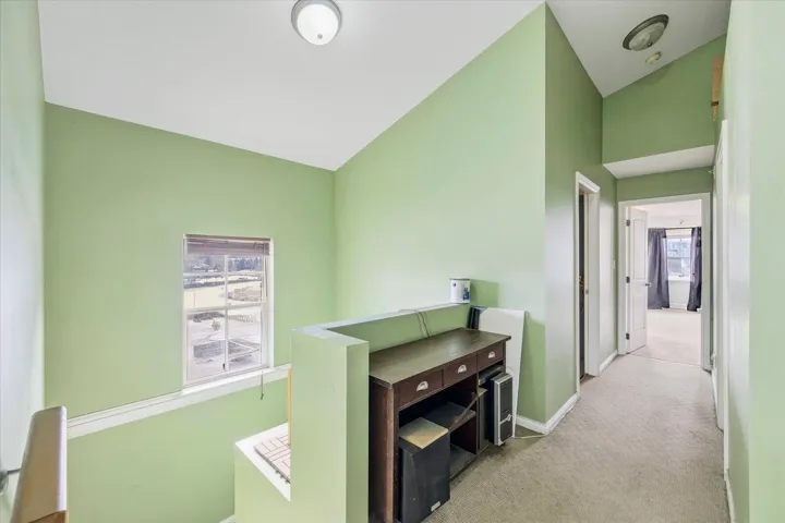 Corridor with lofted ceiling and light colored carpet