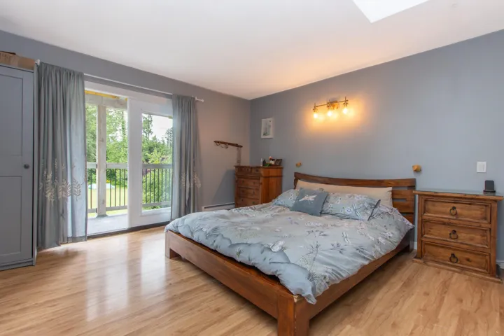 Bedroom featuring covered balcony over looking yard, light wood-type flooring & skylight.