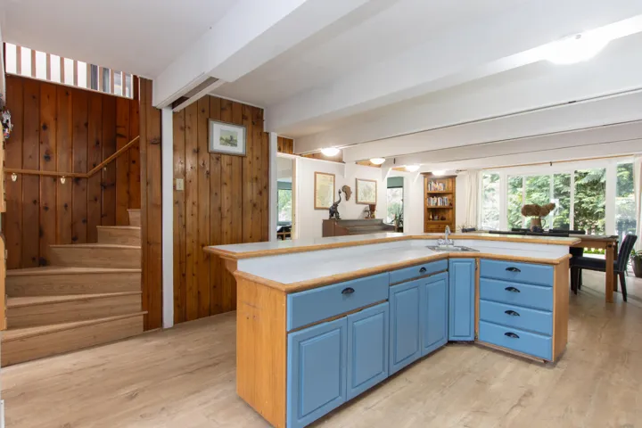 Kitchen with blue cabinetry, beamed ceiling, light countertops, light wood-style flooring, and a kitchen island with sink