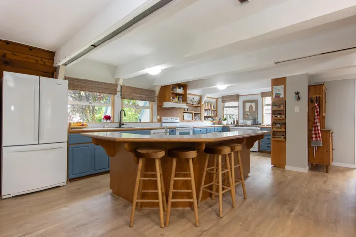 Kitchen featuring white appliances, blue cabinets, light wood-style flooring, beamed ceiling, and a breakfast bar area