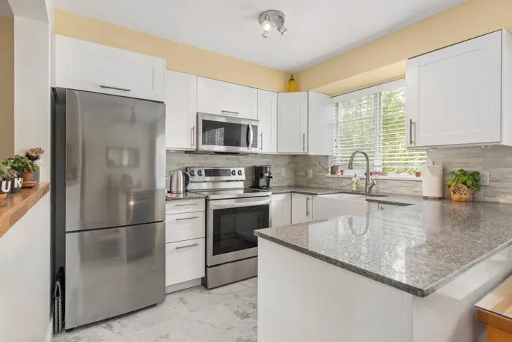 Kitchen featuring appliances with stainless steel finishes, a peninsula, stone counters, and white cabinetry