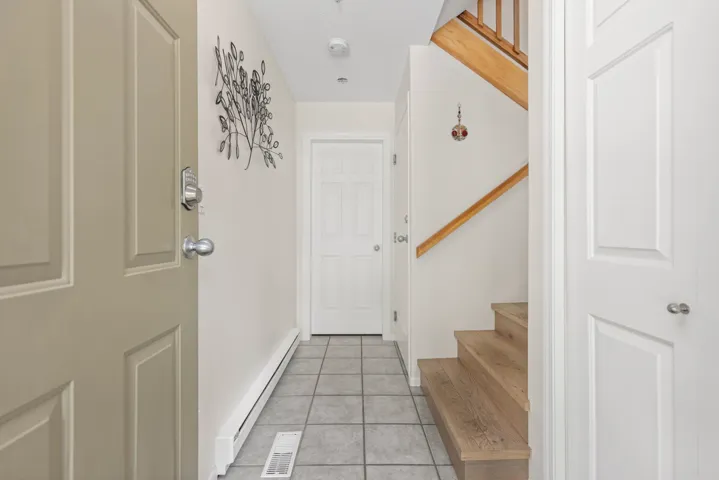 Foyer entrance featuring baseboard heating, stairs, and light tile patterned floors