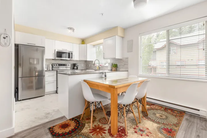 Kitchen featuring appliances with stainless steel finishes, baseboard heating, tasteful backsplash, white cabinets, and light wood-type flooring