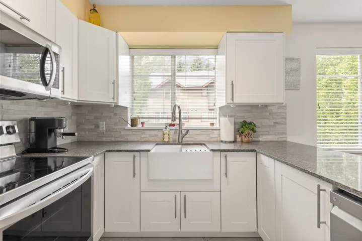 Kitchen with appliances with stainless steel finishes, white cabinetry, tasteful backsplash, and light stone counters