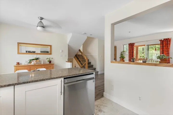 Kitchen featuring stainless steel dishwasher, white cabinets, dark stone counters, light marble finish flooring, and ceiling fan