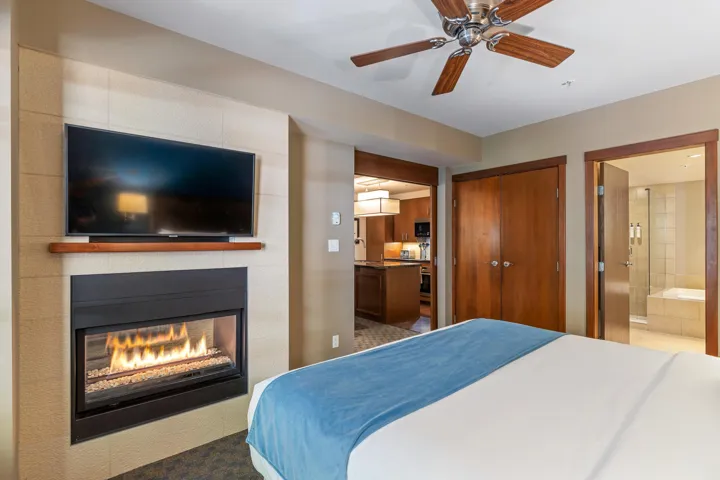 Bedroom featuring a multi sided fireplace, ceiling fan, ensuite bath, and a closet