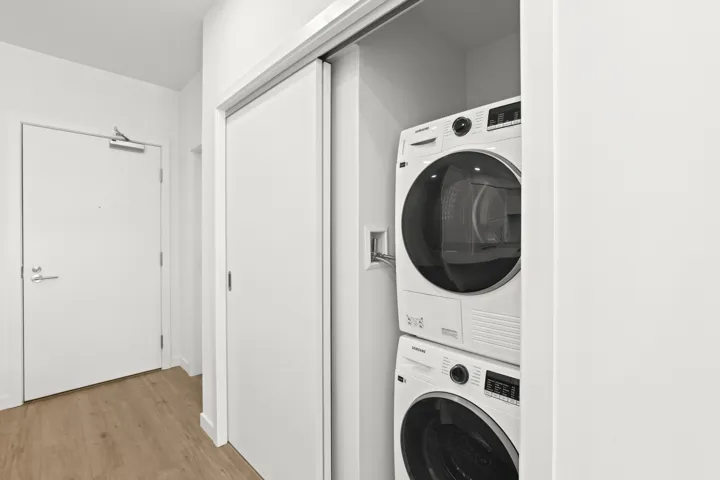 Washroom with stacked washer / dryer and light wood-style floors