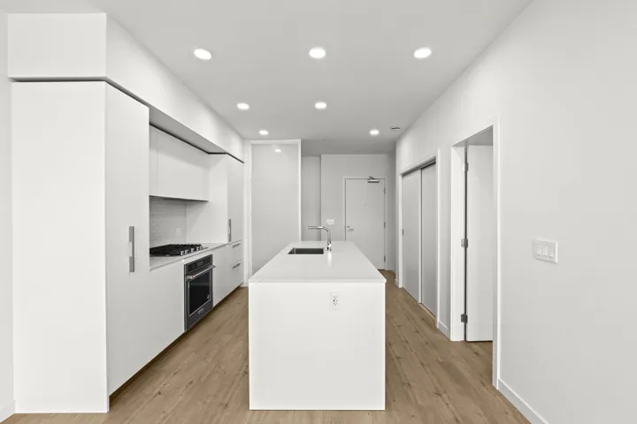Kitchen featuring white cabinets, modern cabinets, light wood-style flooring, an island with sink, and light countertops