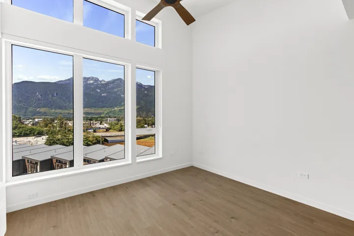 Unfurnished room featuring a mountain view, a ceiling fan, wood finished floors, and a towering ceiling