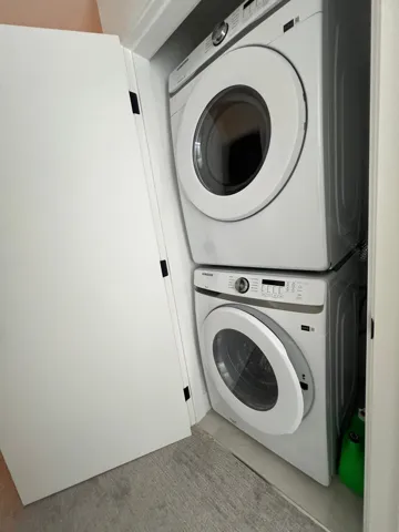 Laundry area with stacked washing machine and dryer and light colored carpet