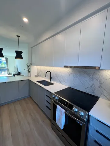 Kitchen with electric stove, decorative light fixtures, white cabinetry, light wood finished floors, and light stone countertops