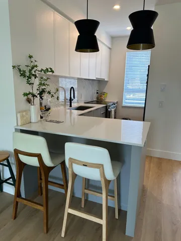 Kitchen featuring a breakfast bar area, a peninsula, backsplash, stainless steel electric range, and light wood-style flooring