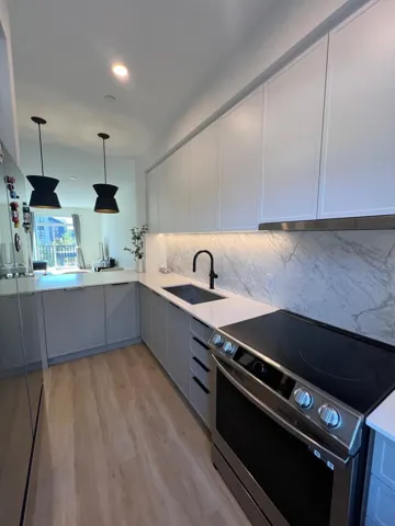 Dual tone kitchen featuring stainless steel appliances, pendant lighting, light wood finished floors, light stone countertops, and tasteful backsplash