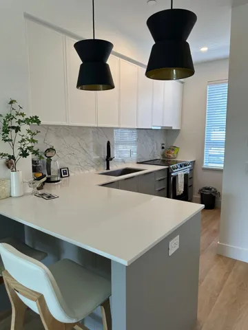 Kitchen featuring a peninsula, electric stove, a kitchen bar, backsplash, and light wood-style flooring