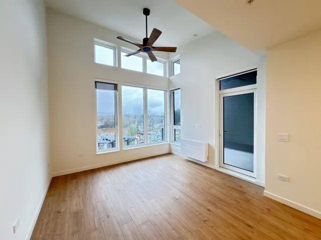 Empty room with light wood-style flooring, a high ceiling, and a ceiling fan