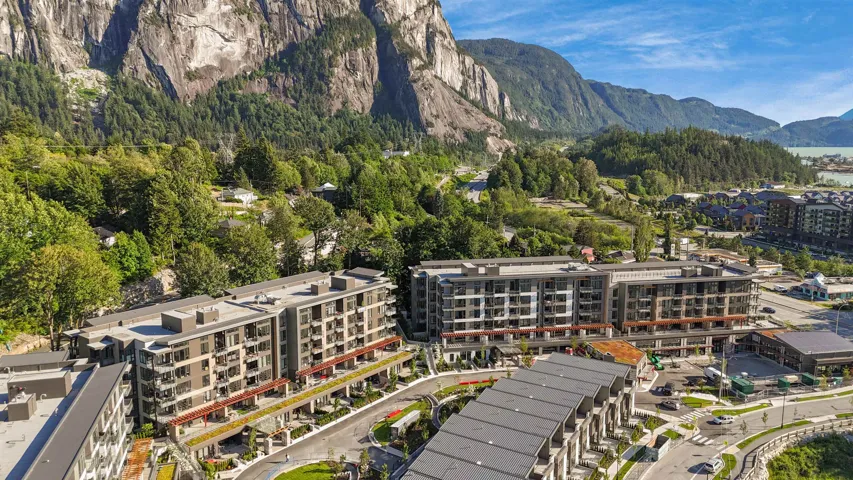 Modern multi-story buildings featuring balconies and green rooftops, set against a backdrop of mountainous terrain