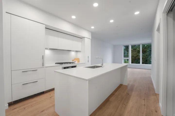 Modern kitchen featuring a large center island with an undermount sink, integrated stainless steel appliances, abundant white cabinetry, and wood-finish flooring