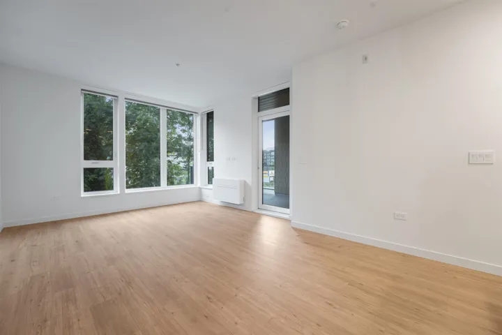 Expansive room featuring wood-finish flooring, a full wall of windows, a white door, white walls, and a wall-mounted climate control unit