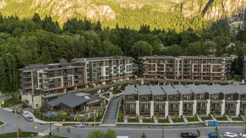 Modern multi-story residential buildings and townhomes featuring balconies, contemporary architectural design, and a mountain backdrop with lush tree coverage