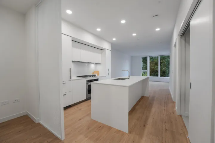 Contemporary kitchen featuring white flat-panel cabinetry, stainless steel appliances, a white tile backsplash, an island with an undermount sink, and wood-finish flooring